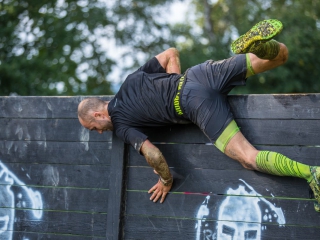 OCR-Athlet beim Überwinden eines Hindernisses Sportler springt über eine Hinderniswand
